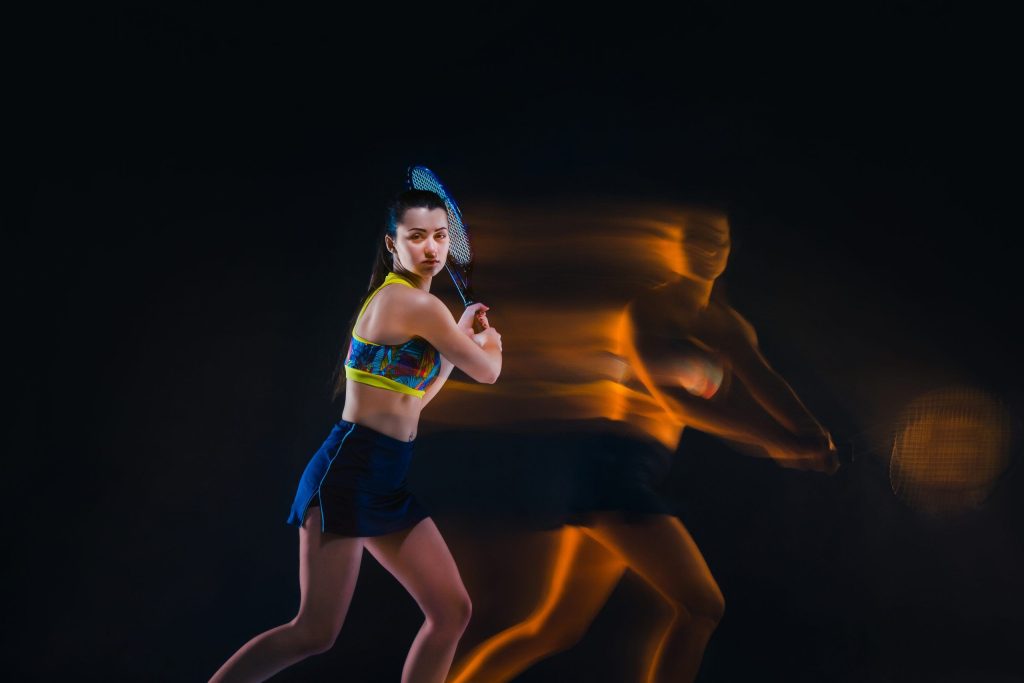 Portrait of beautiful girl tennis player with a racket on dark studio background. Stroboscope shooting technique